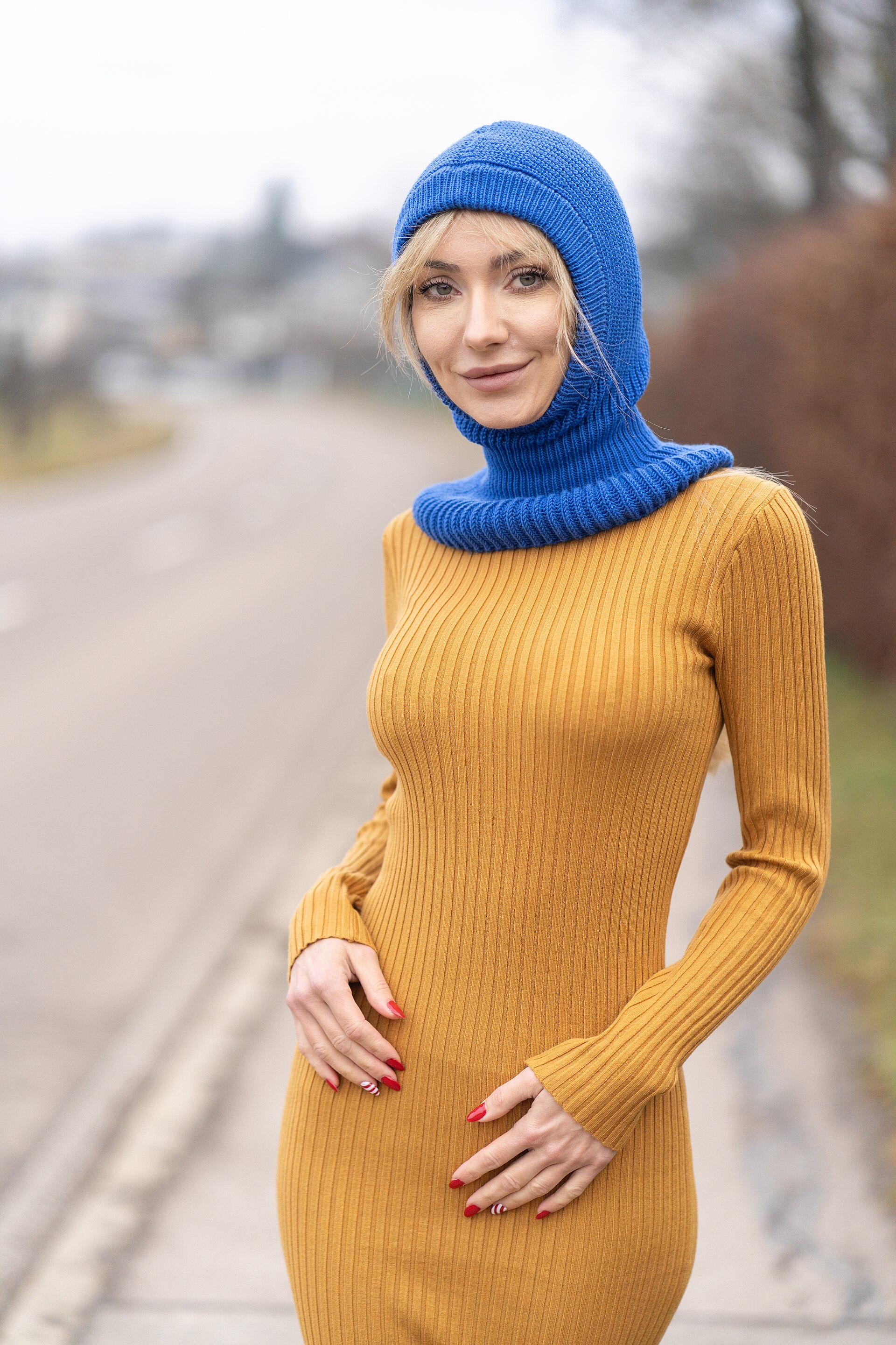 Woman in Mustard Dress | Stylo Aunty A woman poses outdoors in a mustard dress and blue hooded cowl, showcasing winter desi fashion.